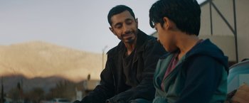 Movie still from “Encounter” (2021), directed by Michael Pearce – A man sitting next to a boy on a street; Close Up shot, Over the shoulder angle