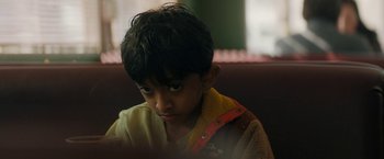 Movie still from “Encounter” (2021), directed by Michael Pearce – A young boy sitting on a couch looking at the camera; Close Up shot, Over the shoulder angle