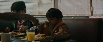 Movie still from “Encounter” (2021), directed by Michael Pearce – A boy sitting at a table eating a sandwich; Medium shot, Over the shoulder angle