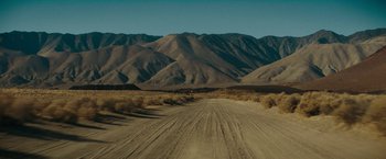 Movie still from “Encounter” (2021), directed by Michael Pearce – A dirt road in the middle of the desert with mountains in the background; Extreme Wide shot, High angle