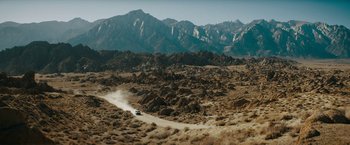 Movie still from “Encounter” (2021), directed by Michael Pearce – A car driving down a dirt road in the middle of the desert; Extreme Wide shot, High angle