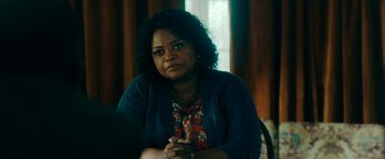 Movie still from “Encounter” (2021), directed by Michael Pearce – A woman sitting in front of a window with her hands clasped together; Close Up shot, Over the shoulder angle