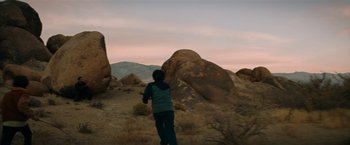 Movie still from “Encounter” (2021), directed by Michael Pearce – A person standing on a dirt field near some rocks; Extreme Wide shot, Low angle