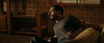 Movie still from “Encounter” (2021), directed by Michael Pearce – A man sitting on the ground in a living room; Medium shot, Low angle