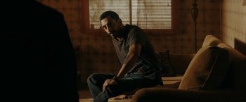 Movie still from “Encounter” (2021), directed by Michael Pearce – A man sitting on the ground in a living room; Medium shot, Low angle