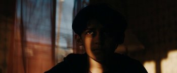 Movie still from “Encounter” (2021), directed by Michael Pearce – A young boy with a hat on looking at the camera; Close Up shot, Low angle