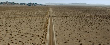 Movie still from “Encounter” (2021), directed by Michael Pearce – An aerial view of an empty road in the middle of the desert; Extreme Wide shot, High angle