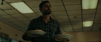 Movie still from “Encounter” (2021), directed by Michael Pearce – A man holding two plates in one hand and a plate in the other hand; Medium shot, Low angle