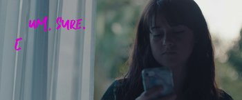 Movie still from “Endings, Beginnings” (2019), directed by Drake Doremus – A woman looking at her cell phone with the text " you are " written above her head; Medium shot, Over the shoulder angle