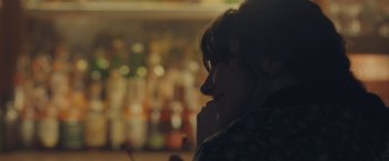 Movie still from “Endings, Beginnings” (2019), directed by Drake Doremus – A woman sitting at a table in front of a bar; Close Up shot, Over the shoulder angle