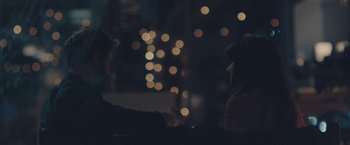 Movie still from “Endings, Beginnings” (2019), directed by Drake Doremus – A man and a woman sitting at a table with lights in the background; Close Up shot, Over the shoulder angle