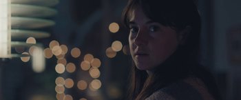 Movie still from “Endings, Beginnings” (2019), directed by Drake Doremus – A woman is looking at the camera with lights in the background; Close Up shot, Over the shoulder angle