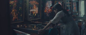 Movie still from “Endings, Beginnings” (2019), directed by Drake Doremus – A woman standing in front of a pinball machine; Medium shot, Over the shoulder angle