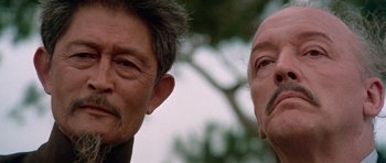 Movie still from “Enter the Dragon” (1973), directed by Robert Clouse – Two older men standing next to each other in front of a tree; Close Up shot, Low angle