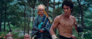 Movie still from “Enter the Dragon” (1973), directed by Robert Clouse – A shirtless man in a headdress stands in front of another man in an oriental costume; Medium shot, Low angle