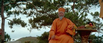 Movie still from “Enter the Dragon” (1973), directed by Robert Clouse – An older man in an orange robe sitting in front of a tree; Wide shot, Low angle
