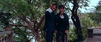 Movie still from “Enter the Dragon” (1973), directed by Robert Clouse – Two men in suits standing next to a tree; Medium shot, Low angle