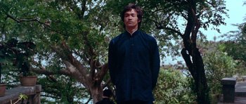 Movie still from “Enter the Dragon” (1973), directed by Robert Clouse – A man standing in front of a large tree; Medium shot, Low angle