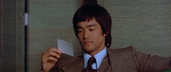 Movie still from “Enter the Dragon” (1973), directed by Robert Clouse – A man in a suit and tie holding a piece of paper; Close Up shot, Low angle