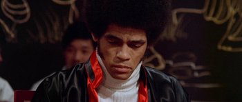 Movie still from “Enter the Dragon” (1973), directed by Robert Clouse – A man with a black jacket and a red ribbon around his neck; Close Up shot, Low angle