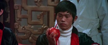 Movie still from “Enter the Dragon” (1973), directed by Robert Clouse – A man holding an apple in his hand; Close Up shot, Over the shoulder angle