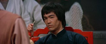 Movie still from “Enter the Dragon” (1973), directed by Robert Clouse – A man sitting in a chair holding a cigarette in his hand; Close Up shot, Low angle