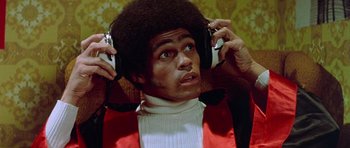 Movie still from “Enter the Dragon” (1973), directed by Robert Clouse – A man in a red jacket is listening to headphones; Close Up shot, Low angle