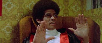 Movie still from “Enter the Dragon” (1973), directed by Robert Clouse – A man in a red and white sweater waves to the camera; Close Up shot, Low angle