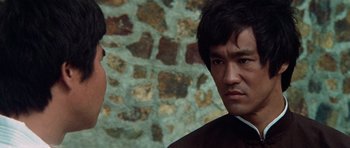 Movie still from “Enter the Dragon” (1973), directed by Robert Clouse – A man in a black shirt and a man in a brown shirt and a brick wall in the background; Close Up shot, Over the shoulder angle