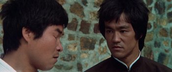 Movie still from “Enter the Dragon” (1973), directed by Robert Clouse – Two asian men standing next to each other in front of a brick wall; Close Up shot, Over the shoulder angle