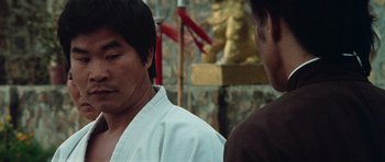 Movie still from “Enter the Dragon” (1973), directed by Robert Clouse – Two men standing next to each other in front of a statue; Close Up shot, Over the shoulder angle