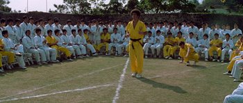 Movie still from “Enter the Dragon” (1973), directed by Robert Clouse – A man in a yellow outfit stands in front of a crowd; Wide shot, Low angle