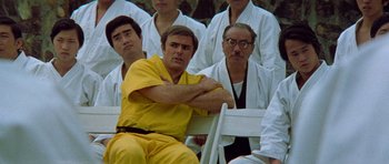 Movie still from “Enter the Dragon” (1973), directed by Robert Clouse – A group of men sitting in a row of chairs; Medium shot, Low angle