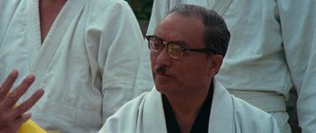 Movie still from “Enter the Dragon” (1973), directed by Robert Clouse – An older man wearing glasses and a white robe; Close Up shot, Low angle