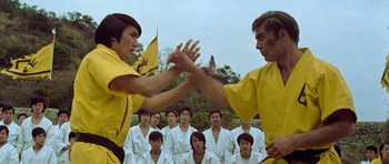 Movie still from “Enter the Dragon” (1973), directed by Robert Clouse – A group of men in white shirts and yellow shirts doing martial arts moves; Medium shot, Low angle