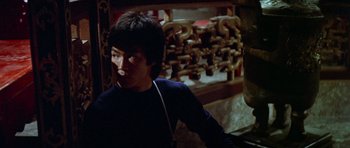 Movie still from “Enter the Dragon” (1973), directed by Robert Clouse – A young man is standing in front of an ornate wall; Medium shot, Low angle