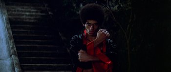 Movie still from “Enter the Dragon” (1973), directed by Robert Clouse – A man in a black and red jacket holding his hands out; Medium shot, Low angle