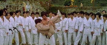 Movie still from “Enter the Dragon” (1973), directed by Robert Clouse – A group of young men in white uniforms holding a man in a white kimono; Wide shot, Low angle