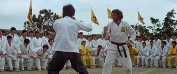 Movie still from “Enter the Dragon” (1973), directed by Robert Clouse – Two men in white shirts and black pants fighting in front of a group of people; Medium shot, Low angle