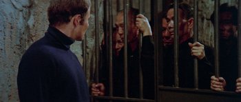 Movie still from “Enter the Dragon” (1973), directed by Robert Clouse – A man standing in front of another man behind bars; Medium shot, Over the shoulder angle