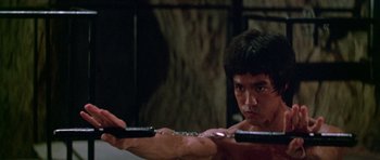 Movie still from “Enter the Dragon” (1973), directed by Robert Clouse – A man is holding a pair of nunchucks in his hands; Medium shot, Low angle
