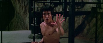 Movie still from “Enter the Dragon” (1973), directed by Robert Clouse – A shirtless man holding a sword and making a hand sign; Medium shot, Low angle