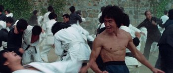 Movie still from “Enter the Dragon” (1973), directed by Robert Clouse – A group of people in white robes and a man in blue shorts; Medium shot, Low angle