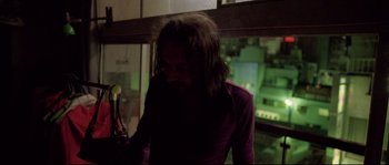 Movie still from “Enter the Void” (2009), directed by Gaspar Noé – A man with long black hair is standing in a dark room; Medium shot, Low angle