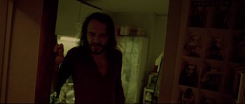 Movie still from “Enter the Void” (2009), directed by Gaspar Noé – A man with long hair standing in a dark room; Medium shot, Low angle