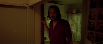 Movie still from “Enter the Void” (2009), directed by Gaspar Noé – A man with long hair and a beard standing in front of a door; Medium shot, Low angle