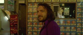 Movie still from “Enter the Void” (2009), directed by Gaspar Noé – A man with long hair and a purple shirt is smiling; Close Up shot, Low angle