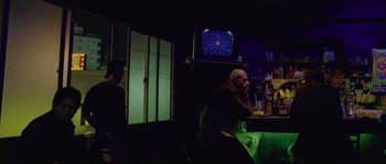 Movie still from “Enter the Void” (2009), directed by Gaspar Noé – A man sitting at a table in front of a television; Wide shot, Low angle