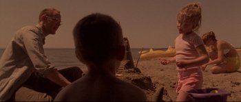 Movie still from “Enter the Void” (2009), directed by Gaspar Noé – A boy sitting on the beach looking at an object in the sand; Wide shot, Over the shoulder angle