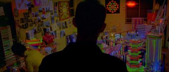 Movie still from “Enter the Void” (2009), directed by Gaspar Noé – A man standing in front of a wall with pictures on the wall; Medium shot, Over the shoulder angle